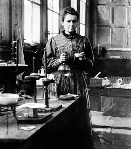 Maria Skłodowska-Curie stojąca w swoim laboratorium z próbówką w ręku